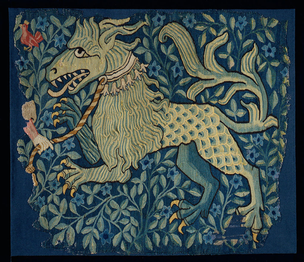 A tapestry lion with a collar and leash against a background of leaves.